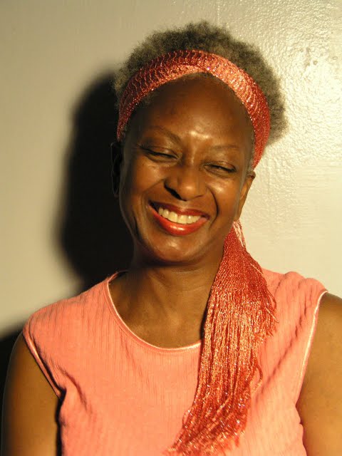 A portrait of Yaa Asantewaa wearing a peach colored blouse and scarf around her hair. She's smiling.